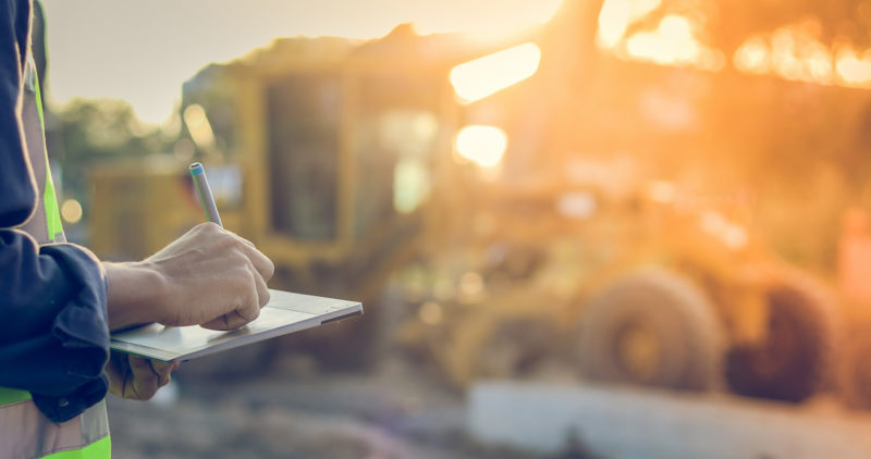 Asian engineer with hardhat using tablet pc computer inspecting and working at construction site